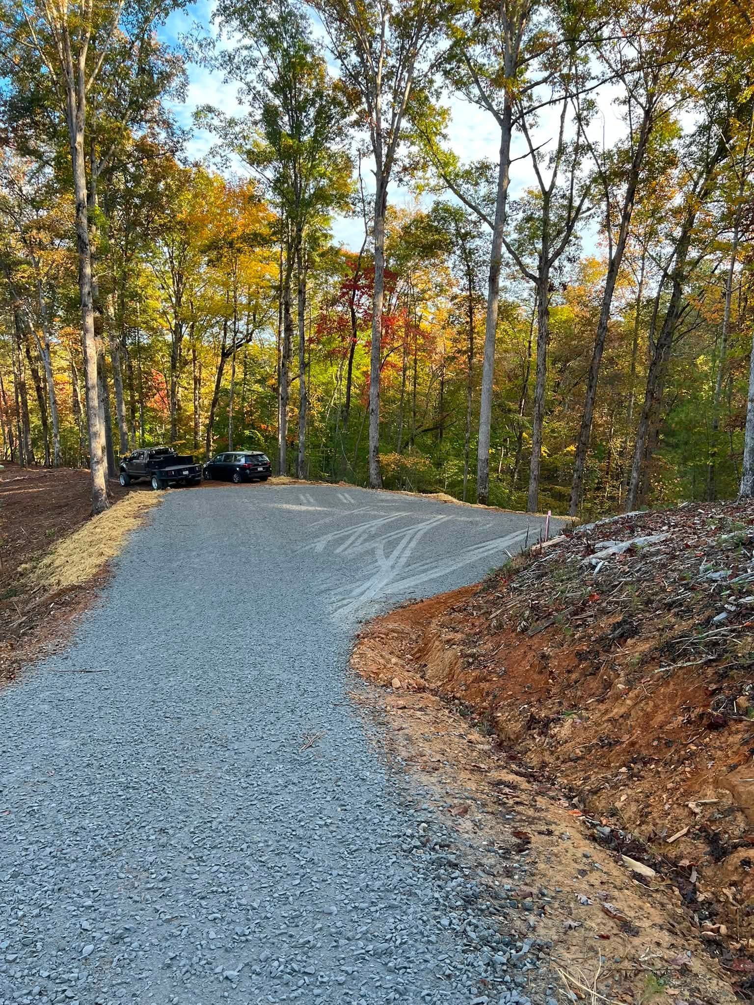 Gravel driveway curving through a wooded autumn landscape with parked cars in the distance
