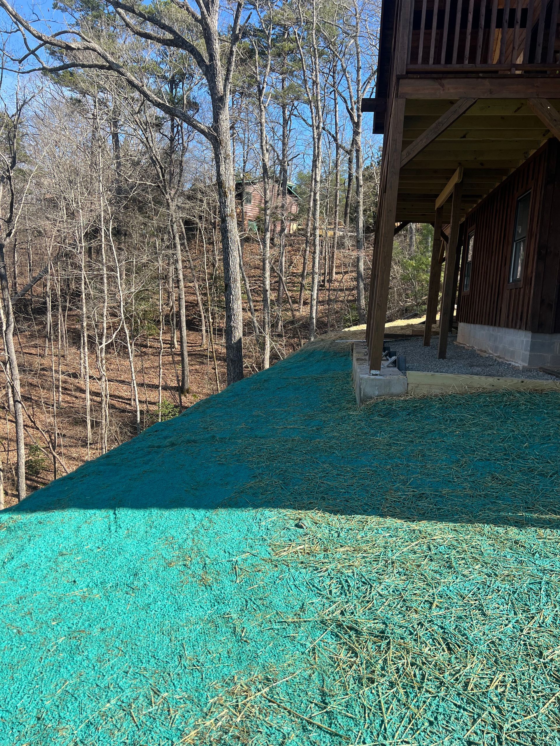 Wooden house deck with bright blue-green gravel beside a wooded hillside.