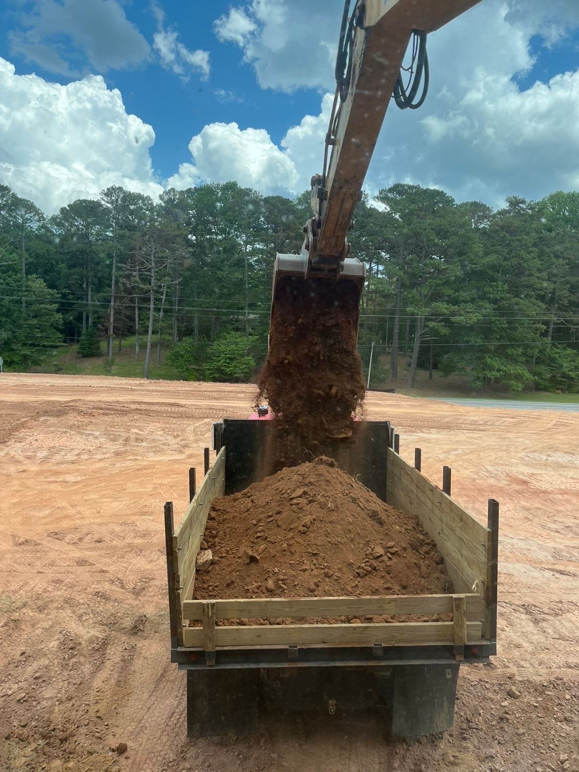 Excavator dumping dirt into a trailer at a construction site under a cloudy sky