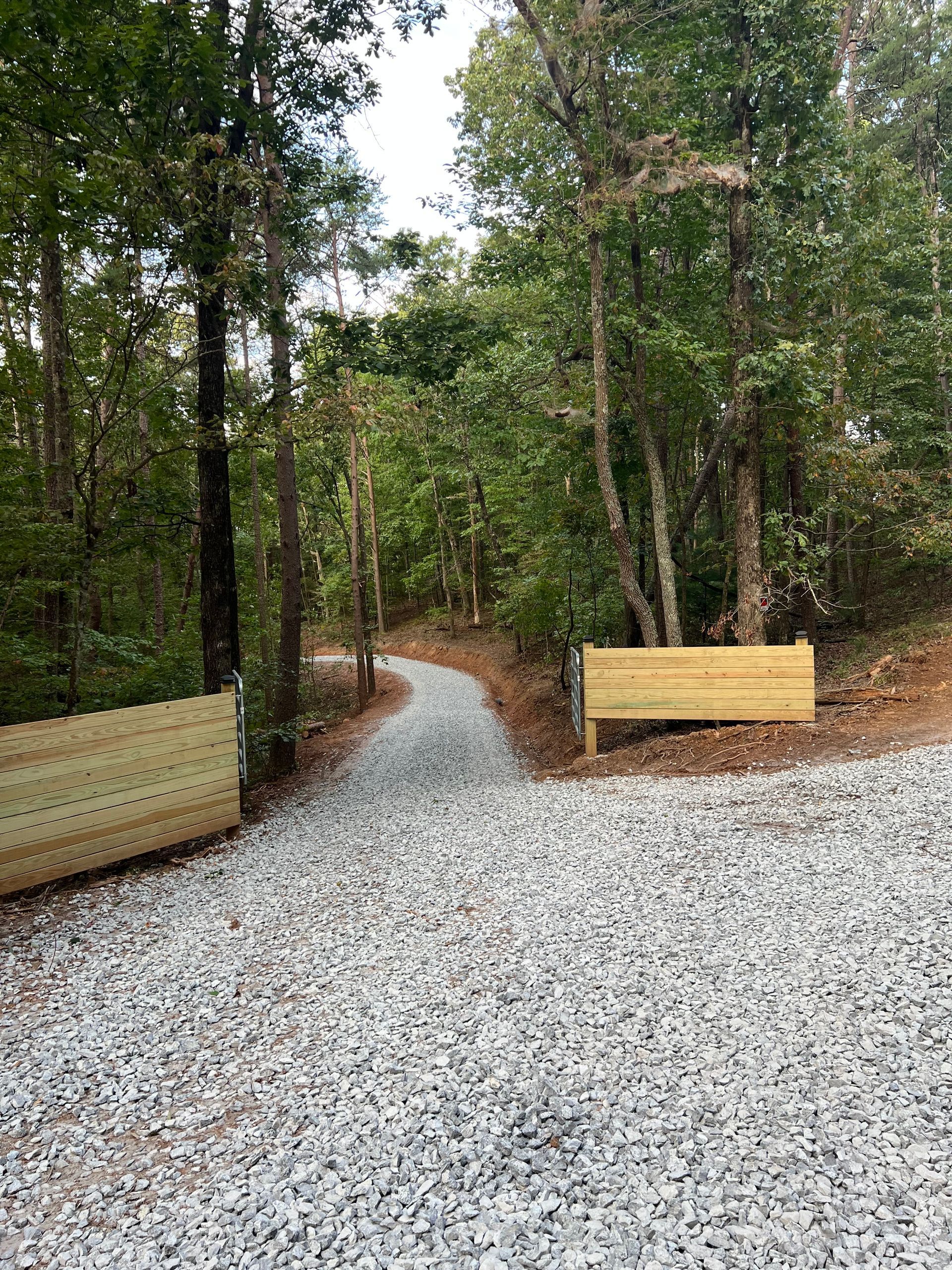 Gravel trail entrance in a wooded park, bordered by wooden benches or barriers on both sides
