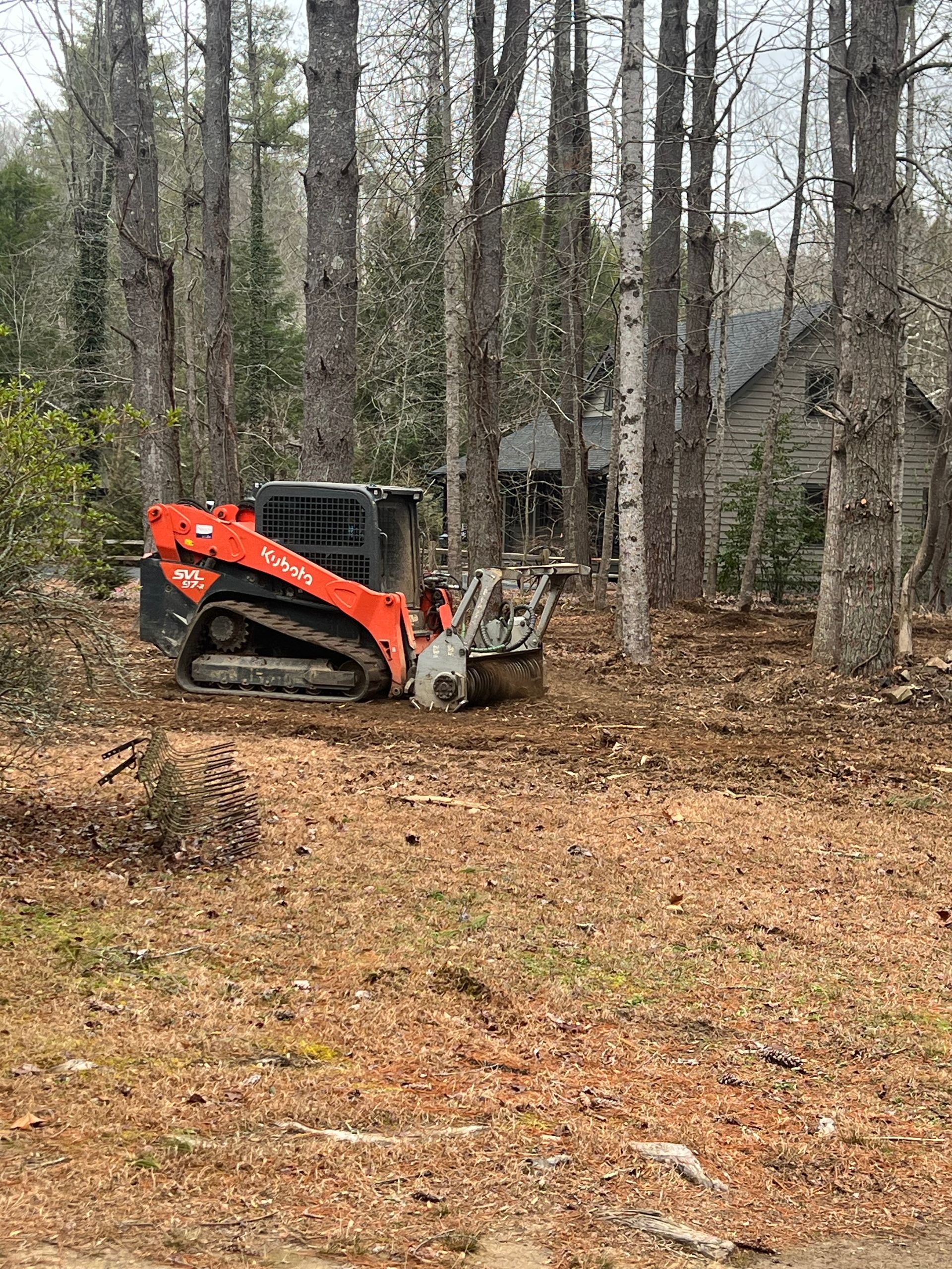 Orange skid steer clearing leaves in a wooded yard near a cabin