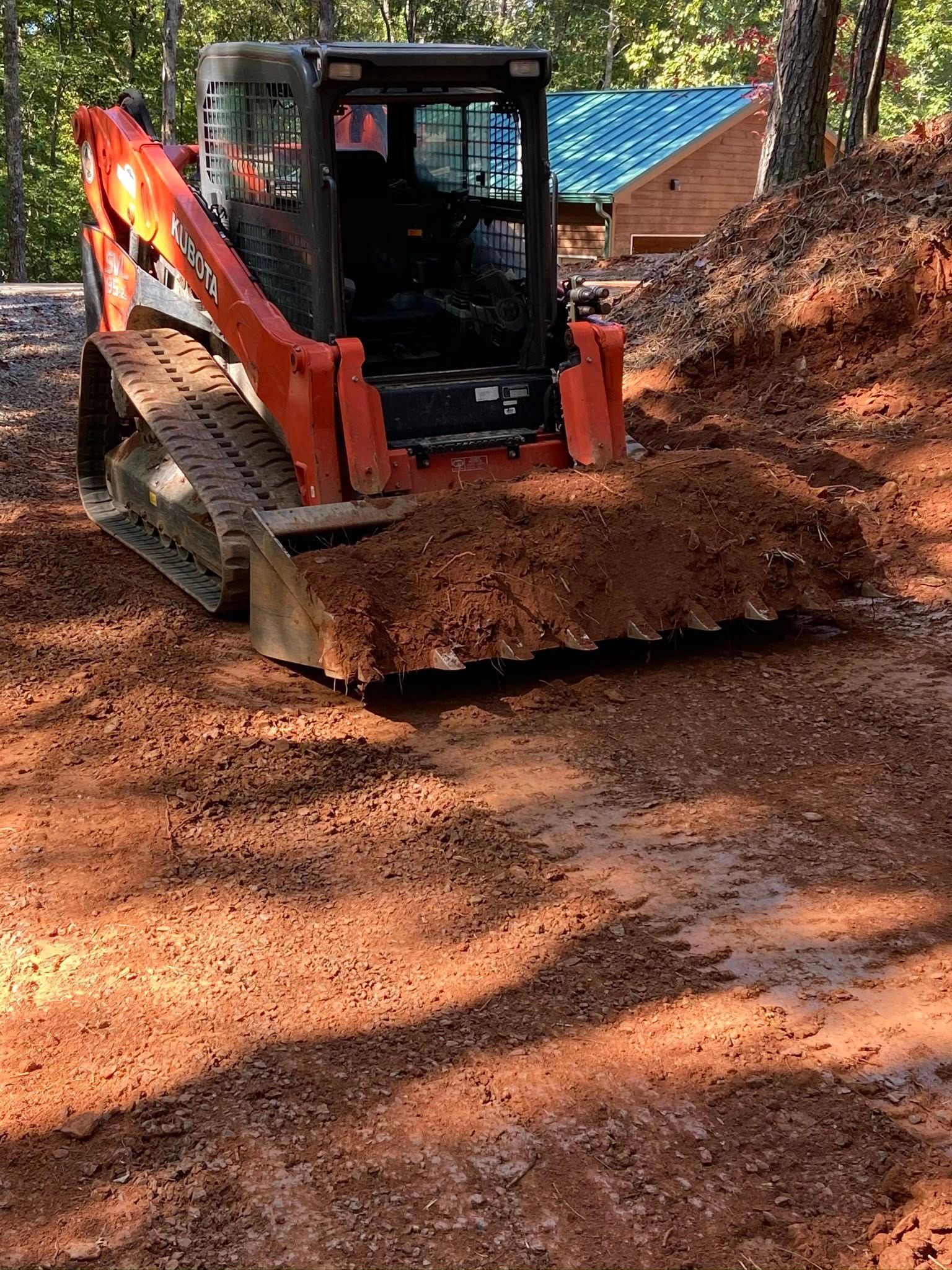 Orange skid-steer loader pushing dirt on a wooded construction path