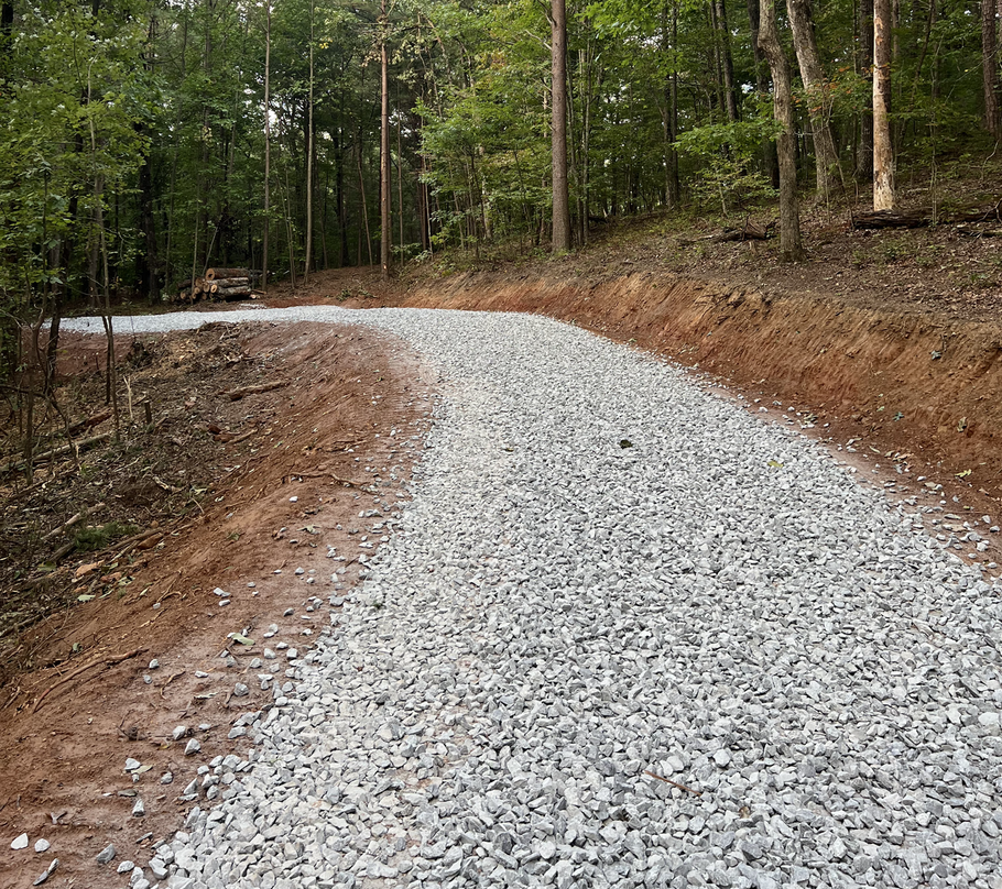 Gravel road curving through a wooded forest with brown dirt edges and green trees