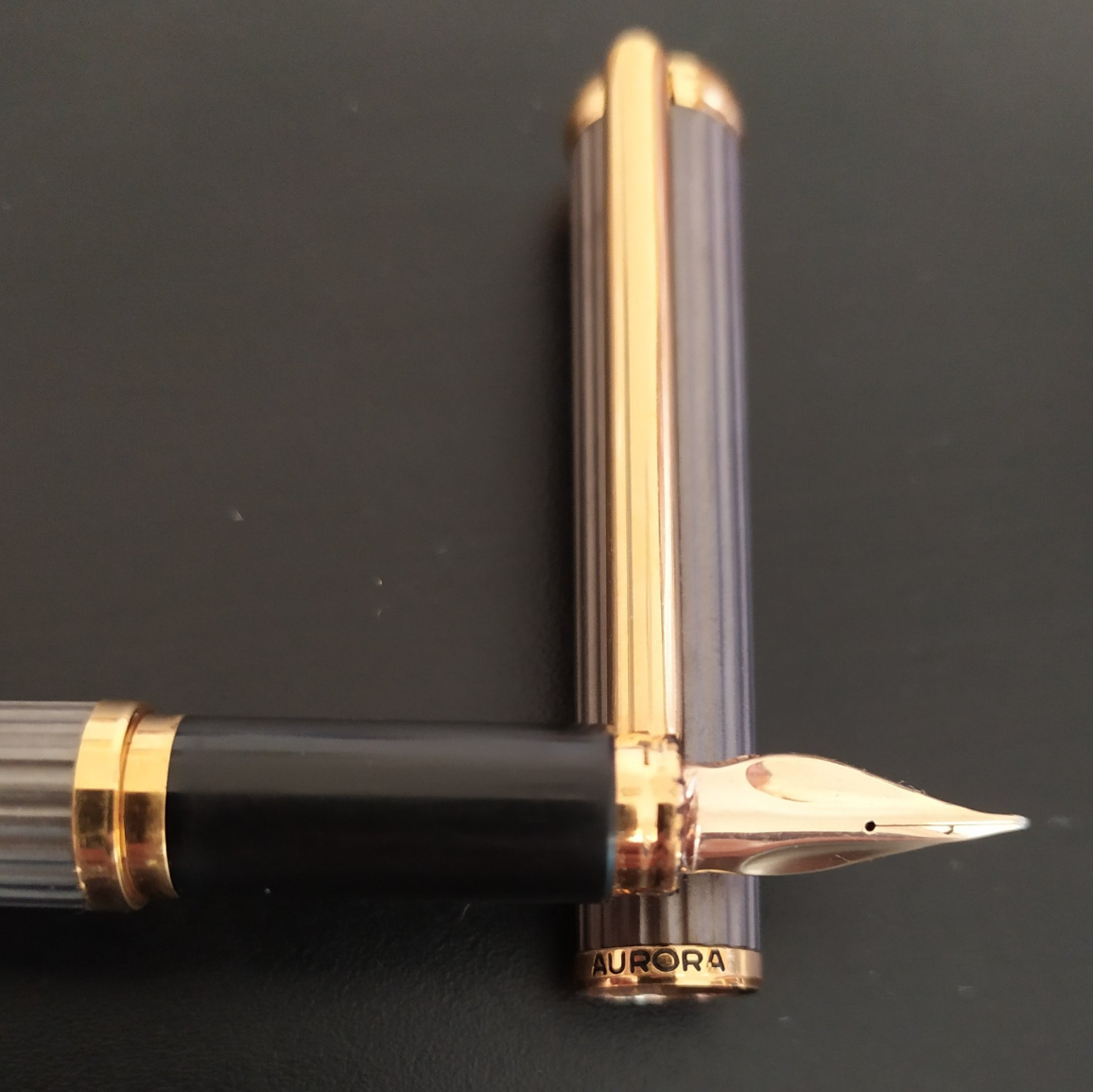 Black and gold fountain pen with cap placed vertically on a dark background