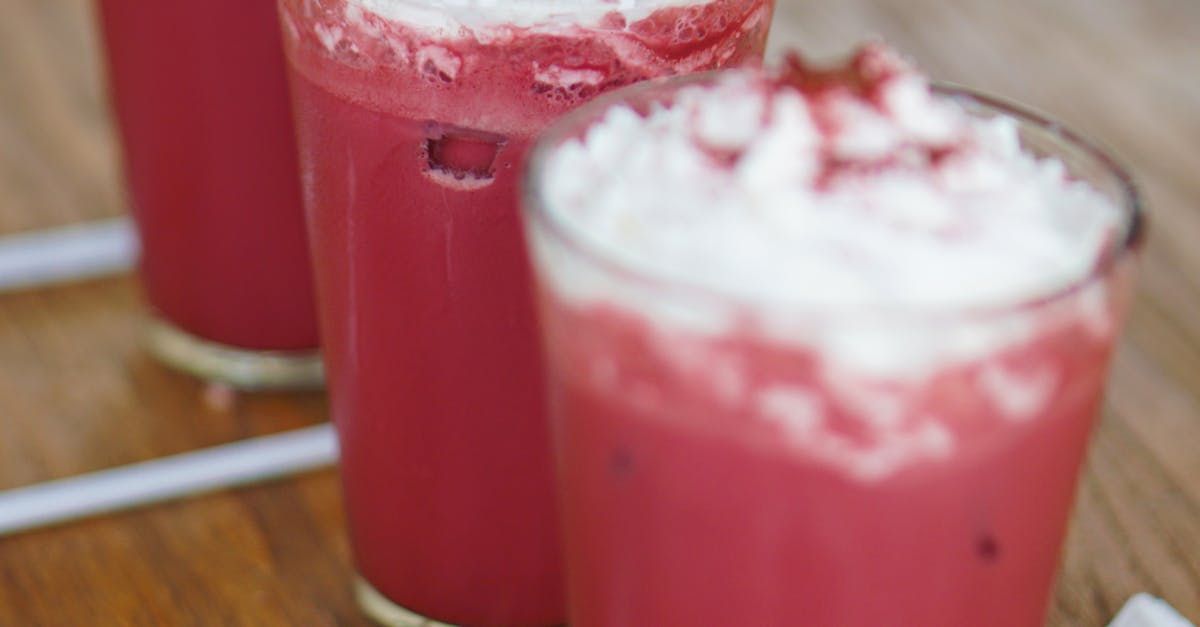 Three glasses of red liquid with whipped cream on top are sitting on a wooden table.
