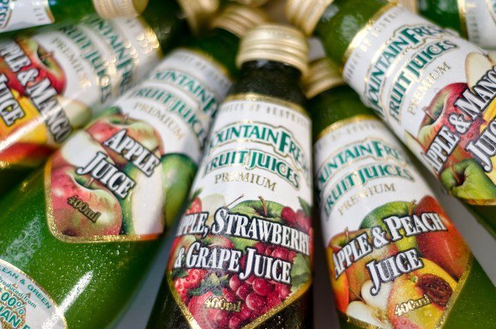 Assorted glass juice bottles with colorful labels, including apple, strawberry grape, and peach, arranged together