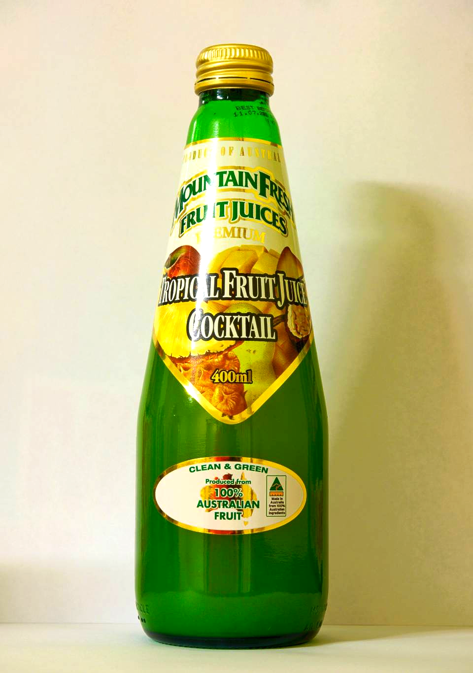 Green glass bottle of fruit cocktail drink with a yellow label and gold cap on a plain background