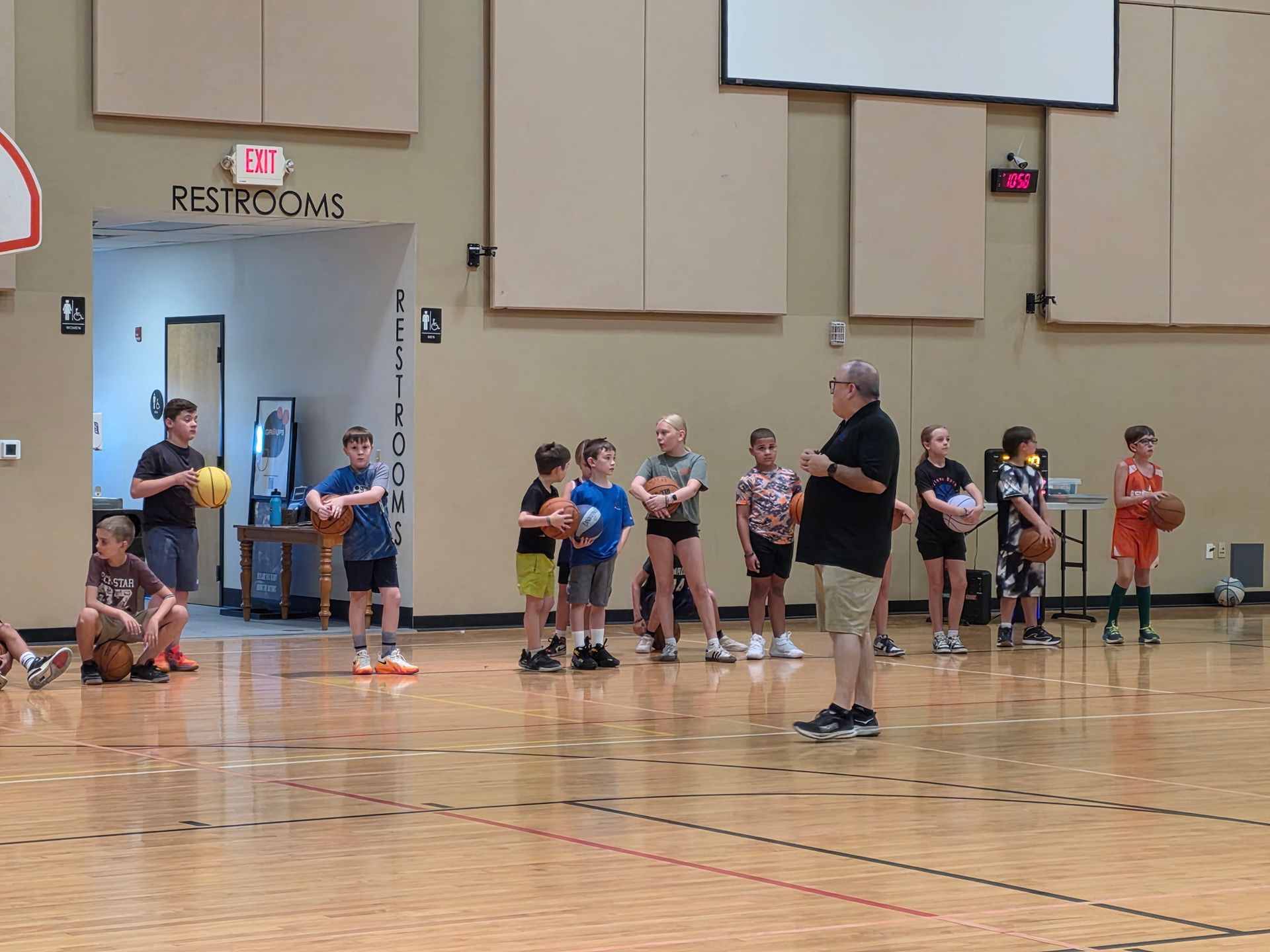 Children lined up in a gym for a basketball drill, with a coach standing nearby.