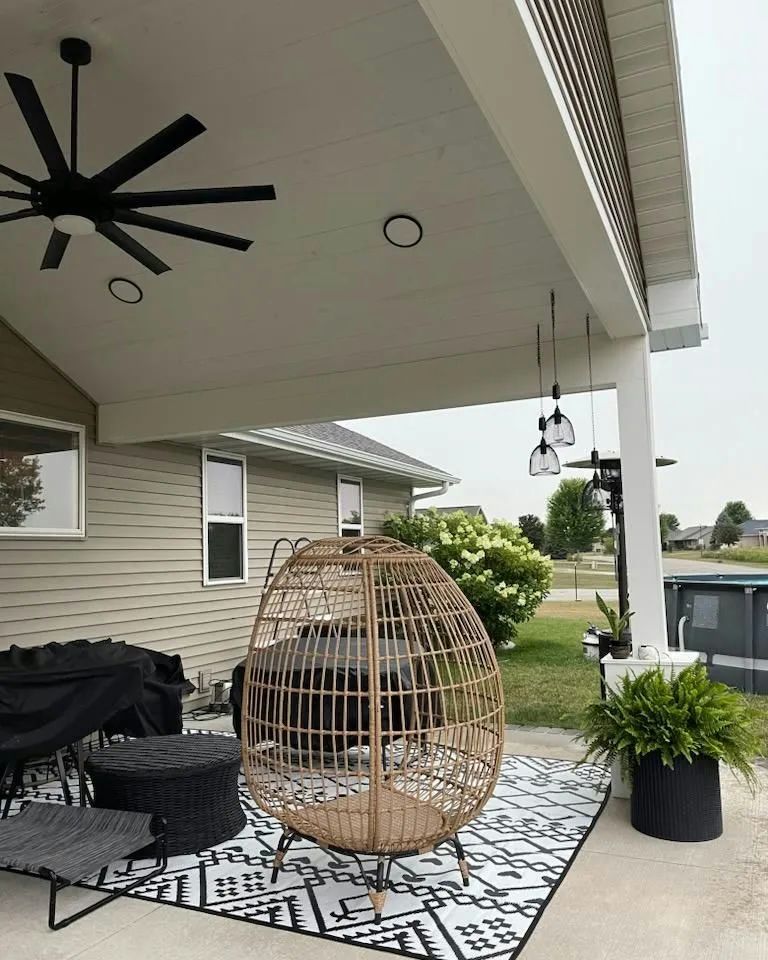 Covered patio with egg chair, seating area, ceiling fan, and black and white patterned rug.
