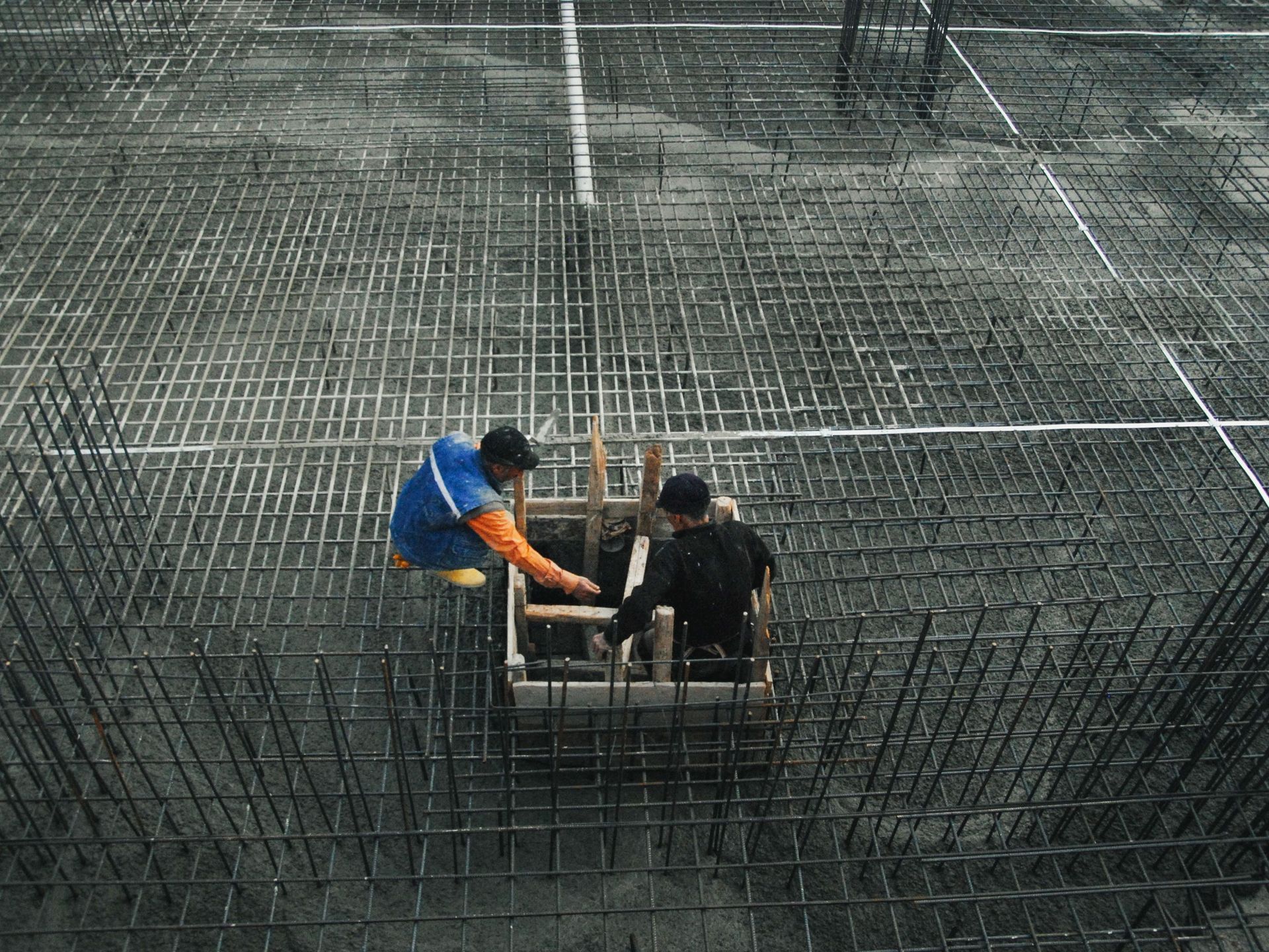 Two workers in blue and black shirts tying rebar on a concrete construction site