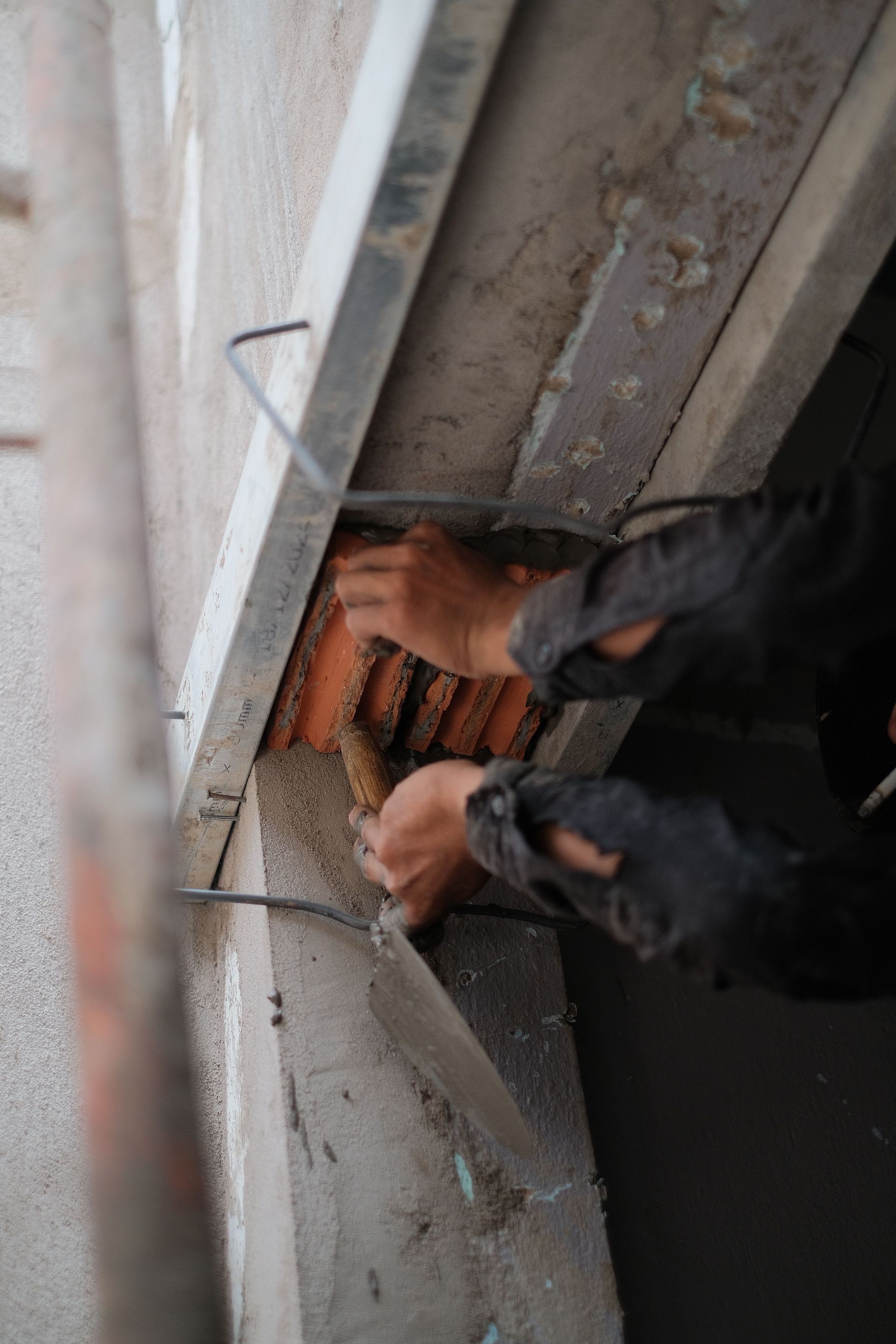 Hand scraping a wall with a blue tool and orange glove during plaster repair