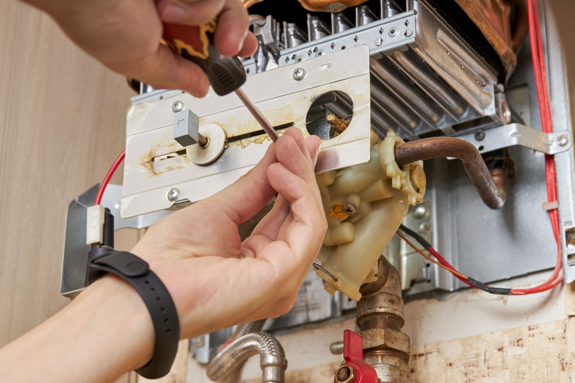 A technician repairing a wall-mounted water heater by adjusting an internal valve with a screwdriver. A technician repairing a wall-mounted water heater by adjusting an internal valve with a screwdriver.