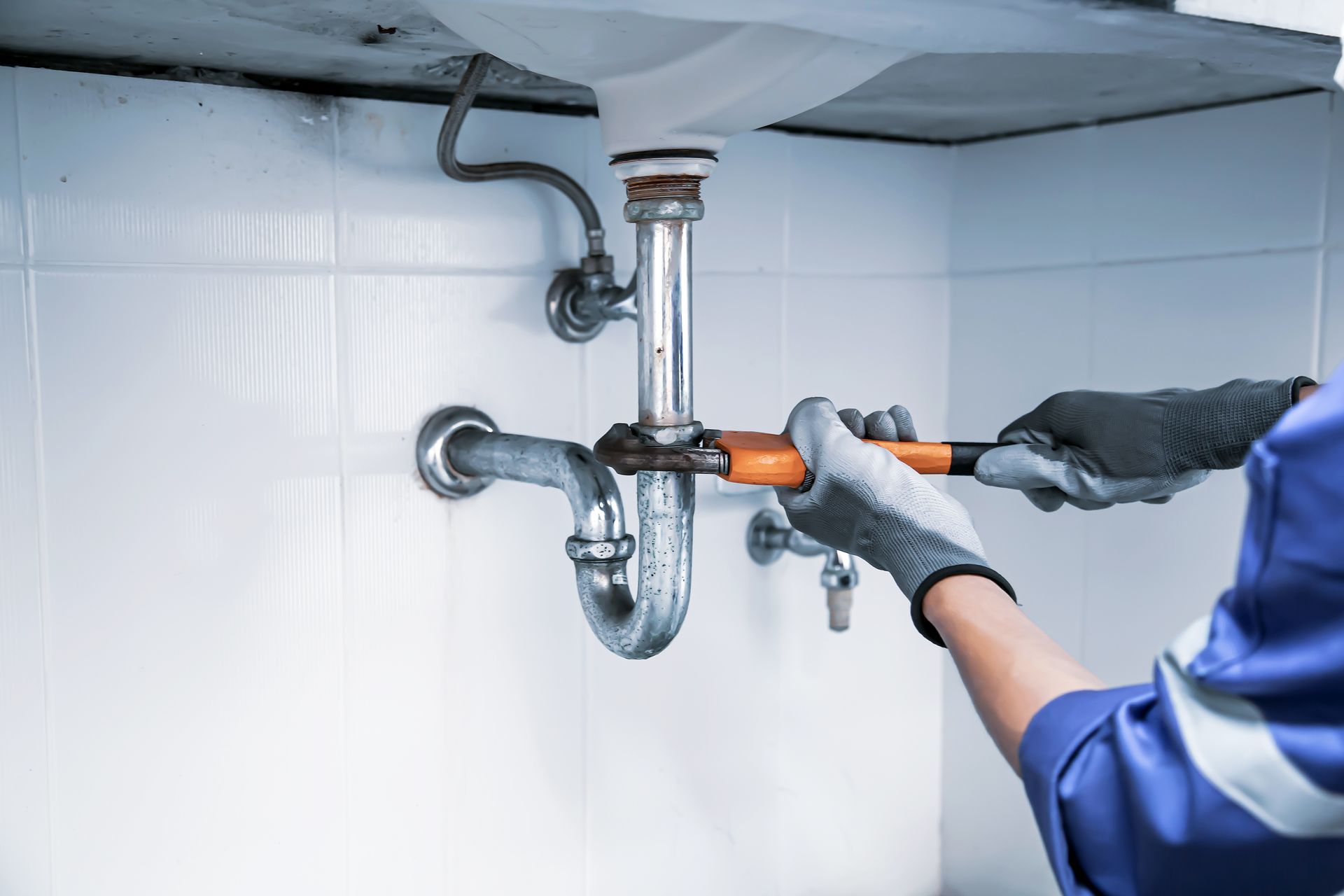 A technician plumber is using a wrench to repair a water pipe under the sink. A technician plumber is using a wrench to repair a water pipe under the sink.
