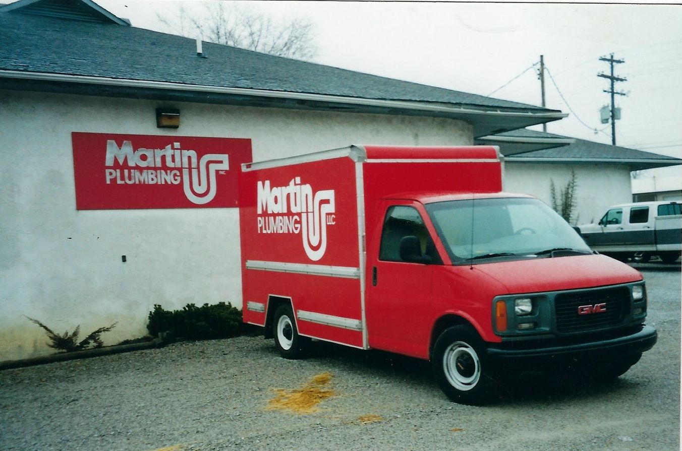 Red Martin Plumbing service truck parked in front of a building with the company's sign.