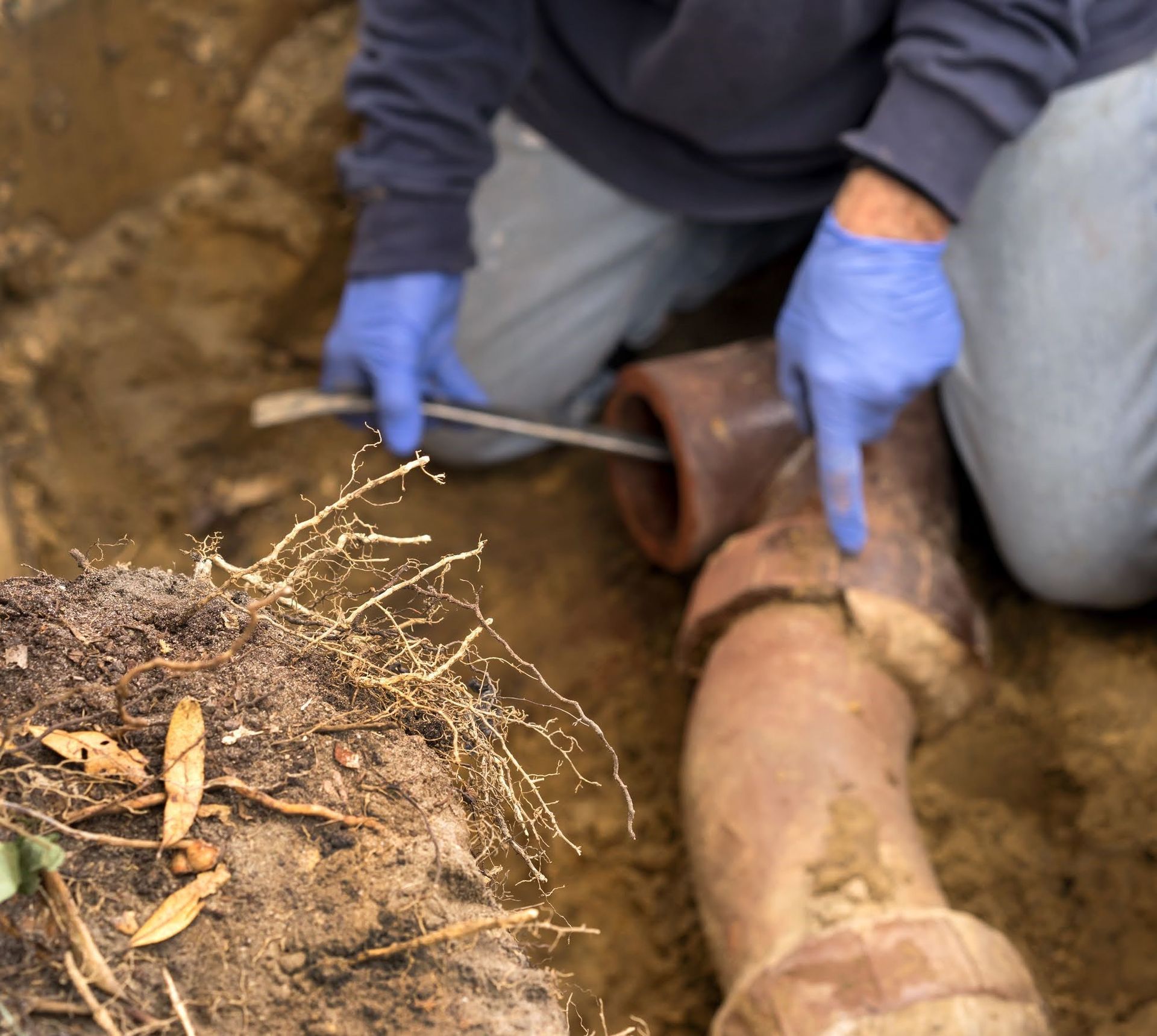 A man wearing blue gloves is working on a pipe in the dirt