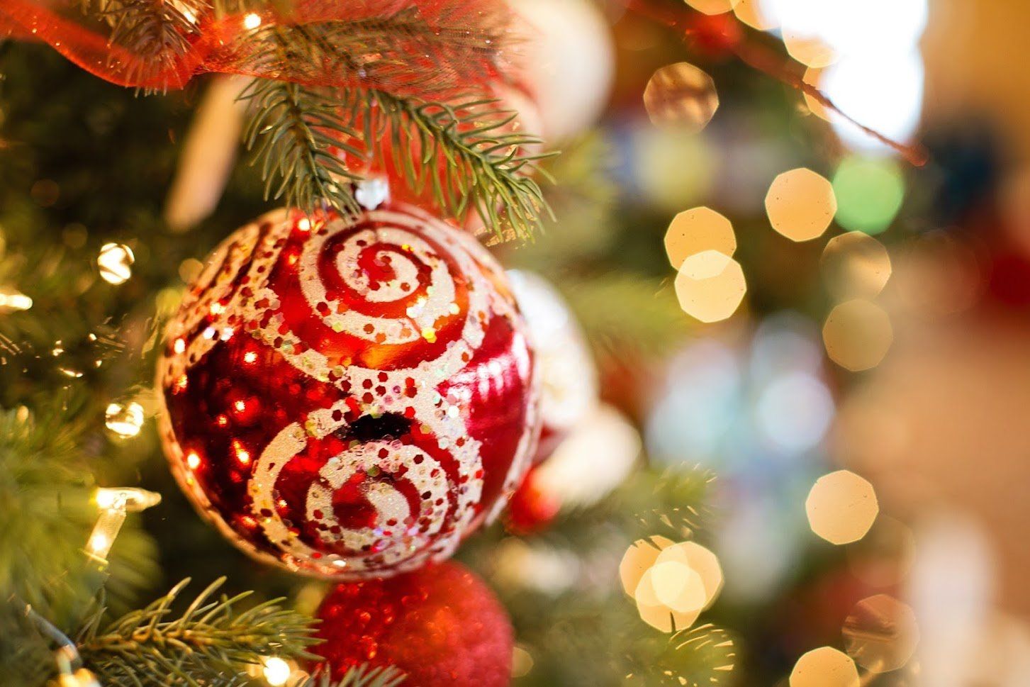A red and white ornament is hanging from a christmas tree.