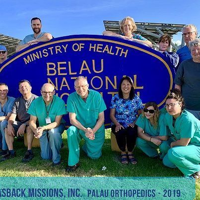A group of people are posing for a picture in front of a sign that says ministry of health belau national hospital.