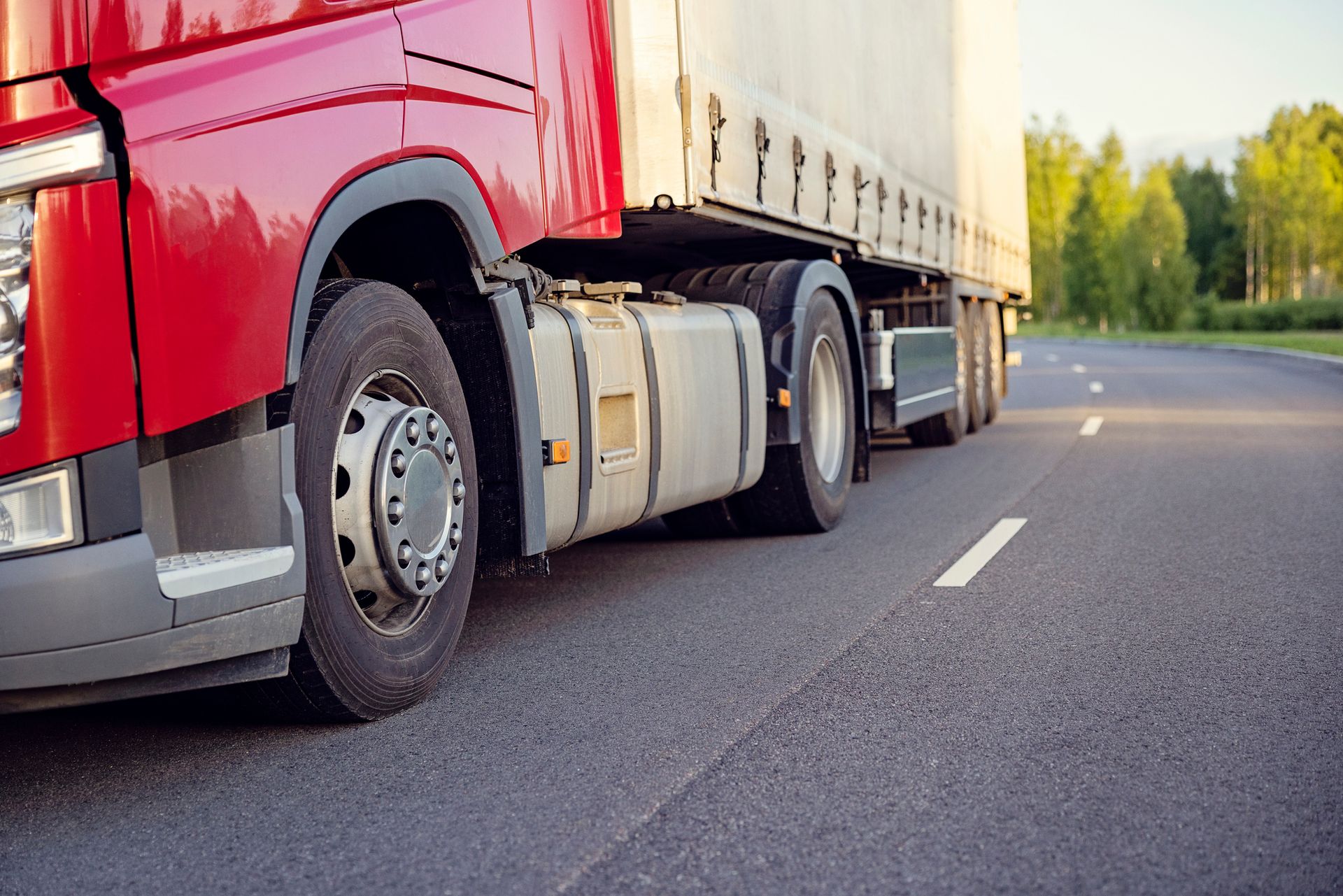 Red semi-truck driving on a paved road, carrying a white cargo trailer.