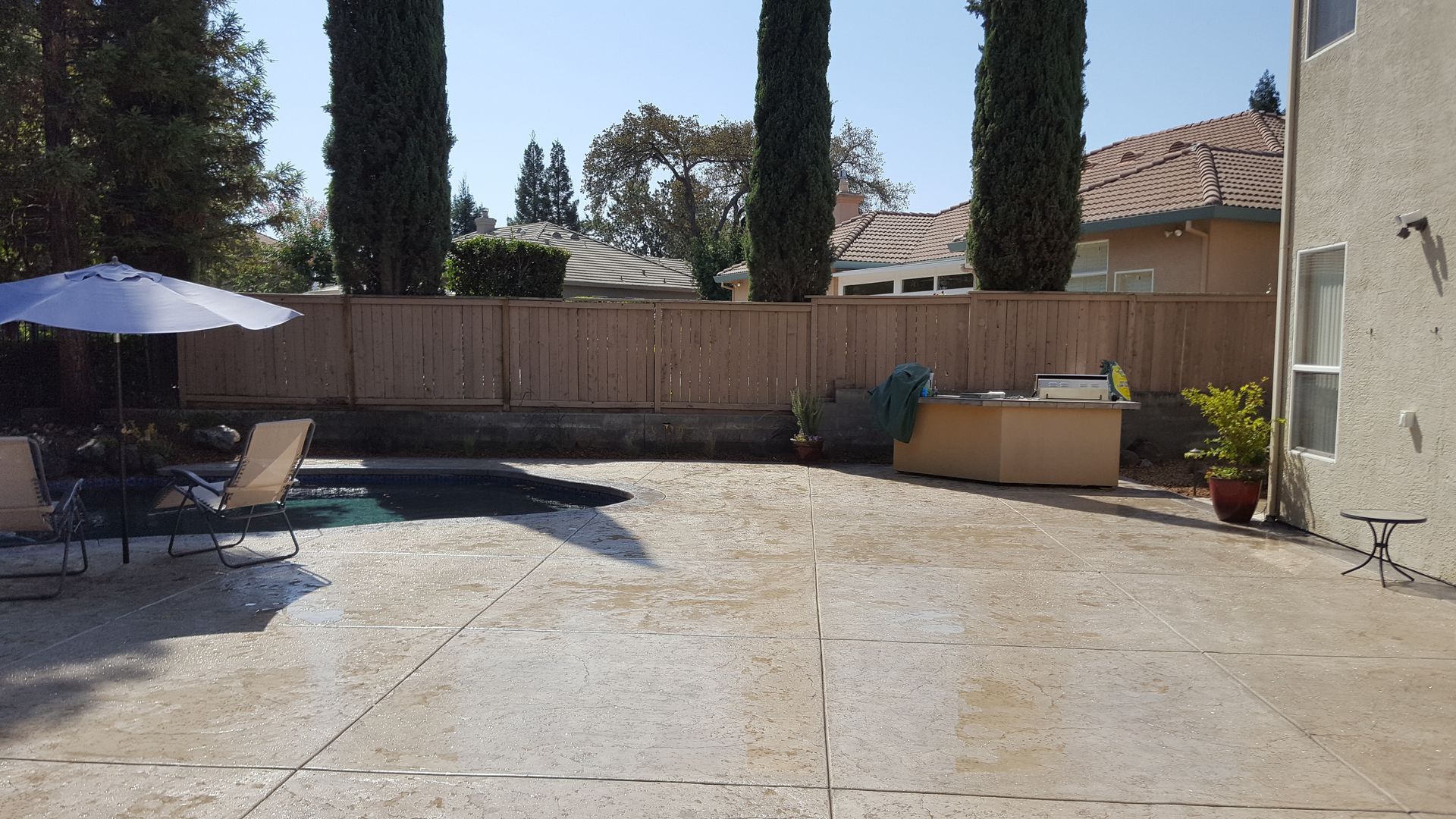 A backyard with a pool , chairs , umbrellas and a fence.