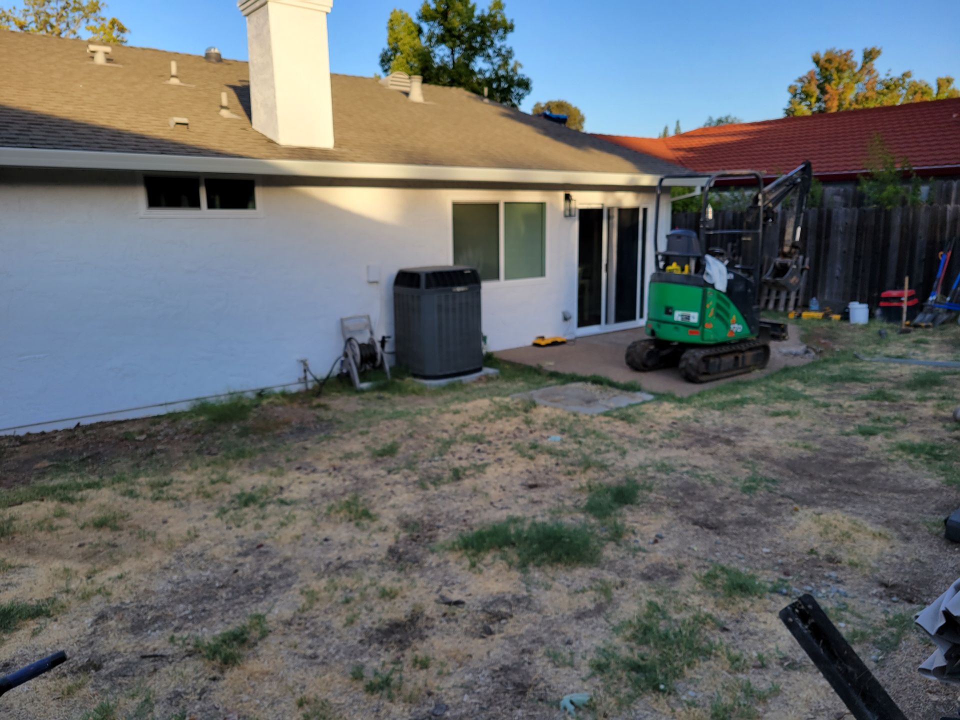 A green excavator is parked in the backyard of a house.
