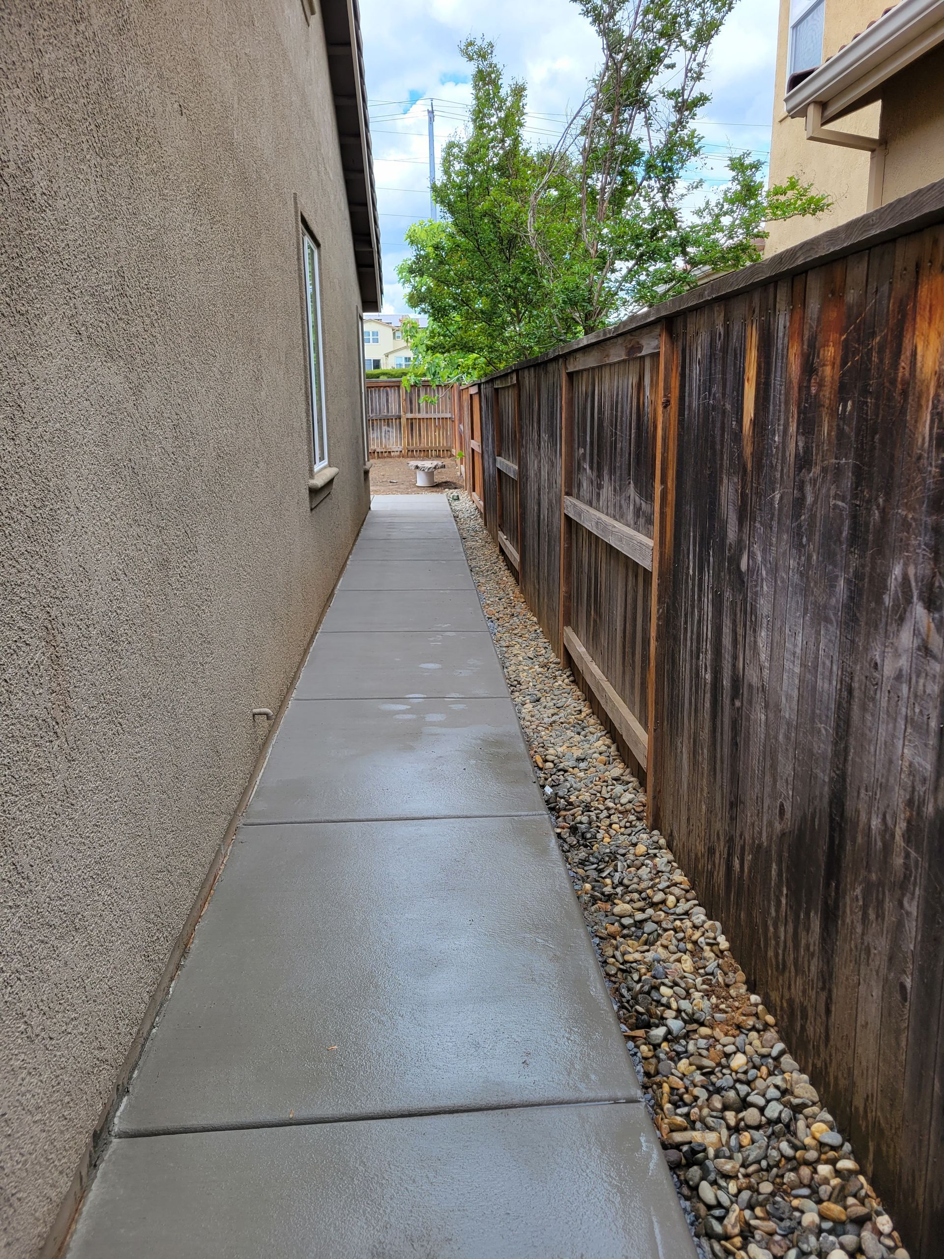 A sidewalk leading to a house next to a wooden fence.