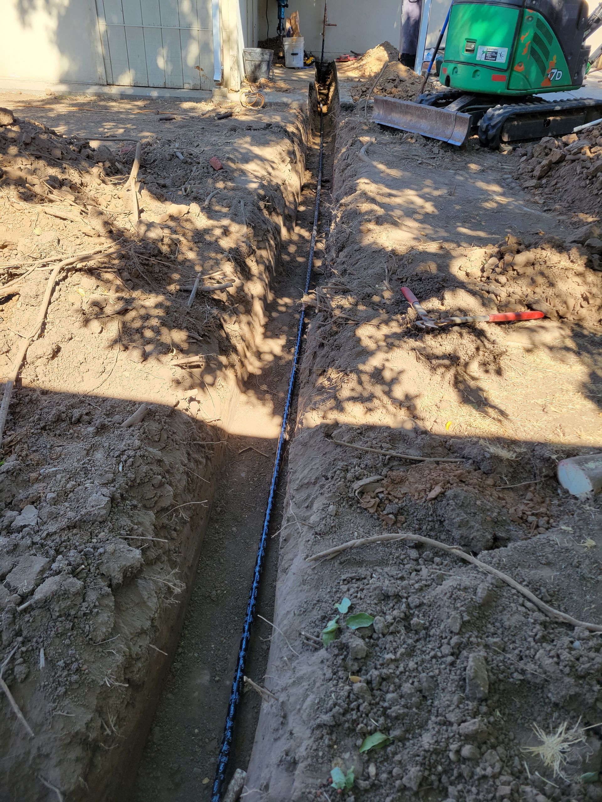 A green excavator is digging a hole in the dirt next to a pipe.