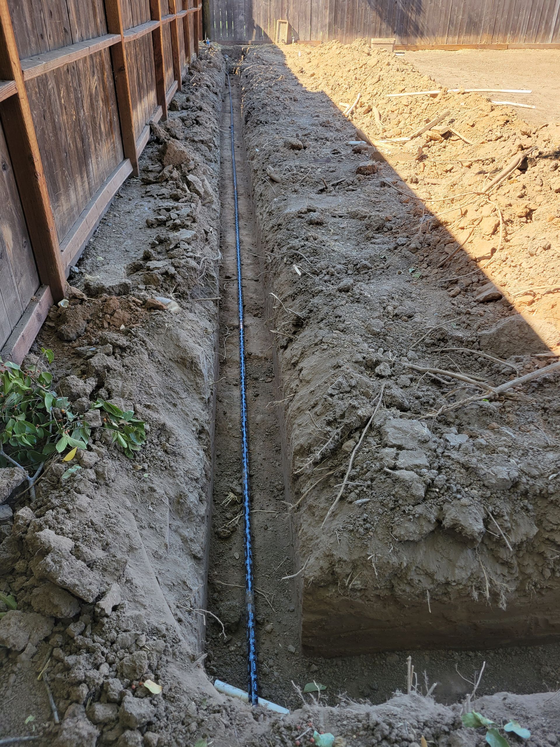 A pipe is being installed in the dirt next to a fence.