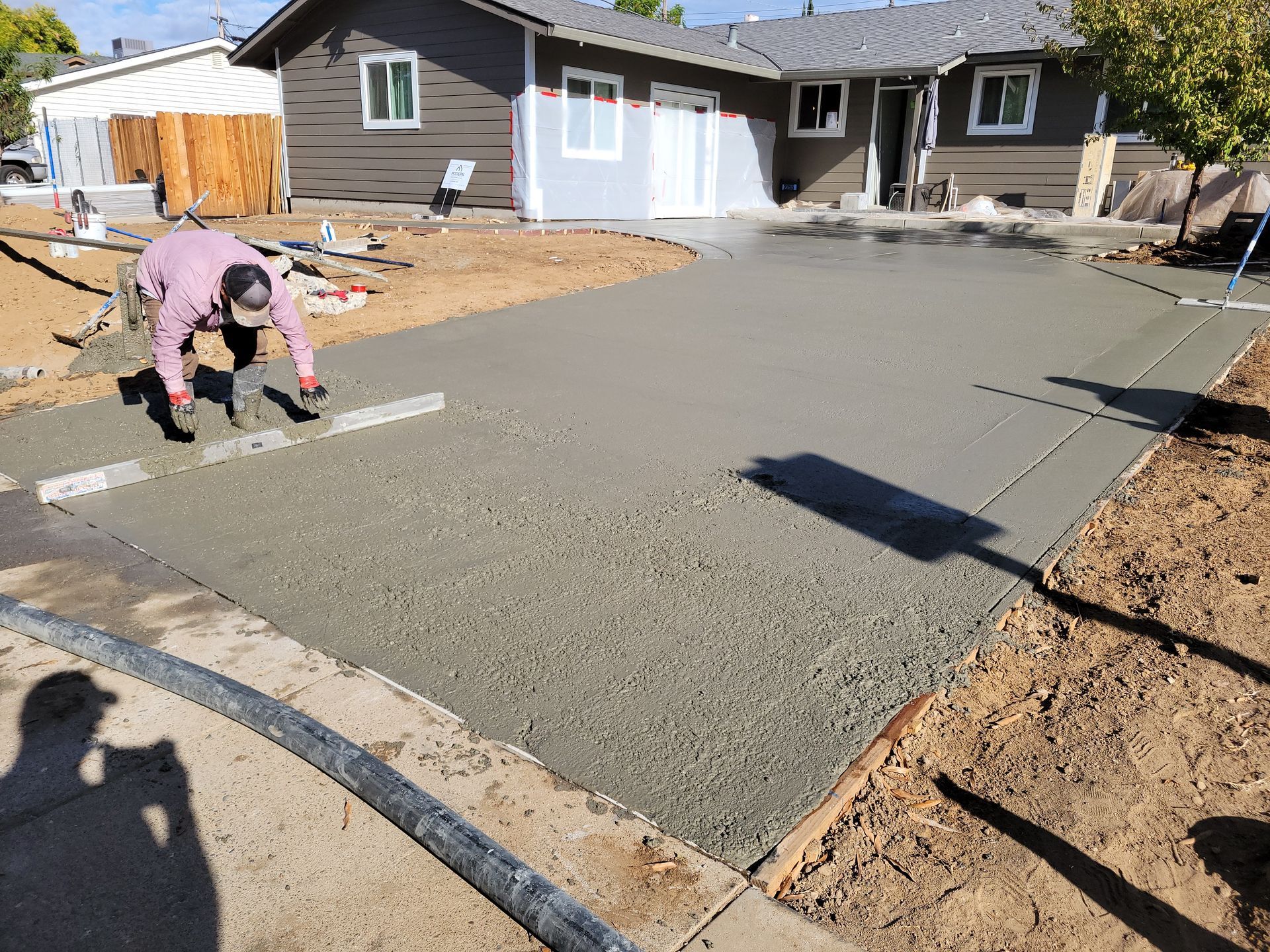 A man is working on a concrete driveway in front of a house.