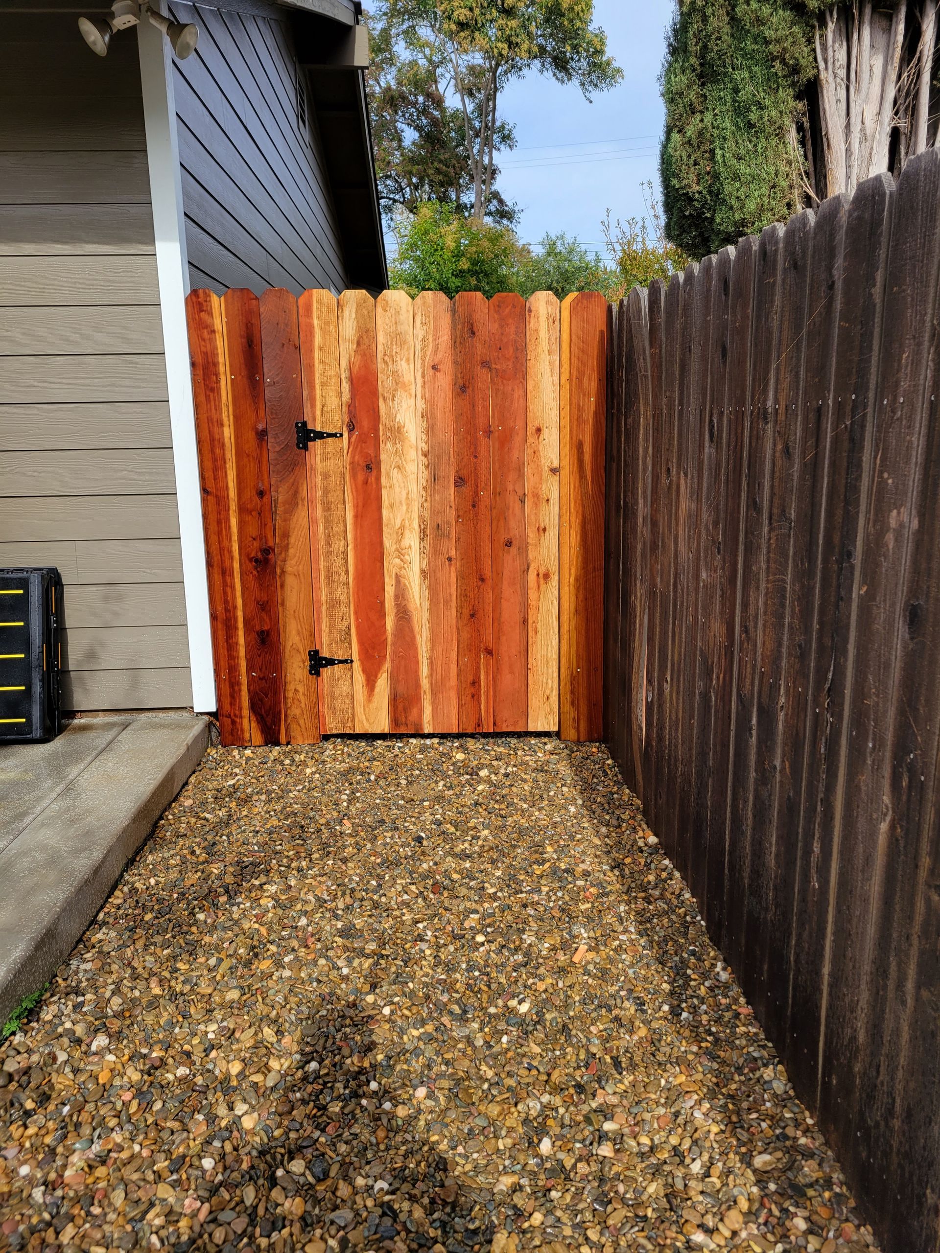 A wooden fence with a gate in the middle of a gravel path.