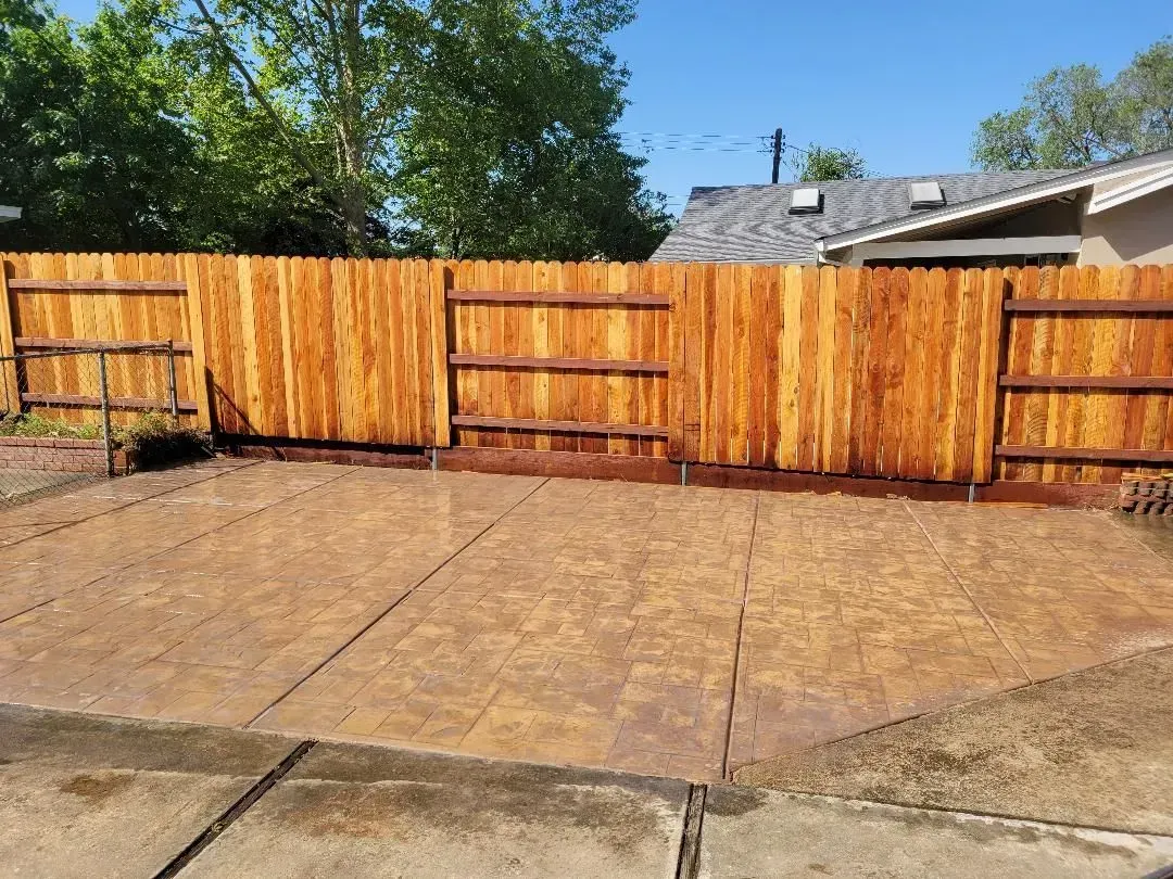 A wooden fence surrounds a concrete driveway in a backyard.