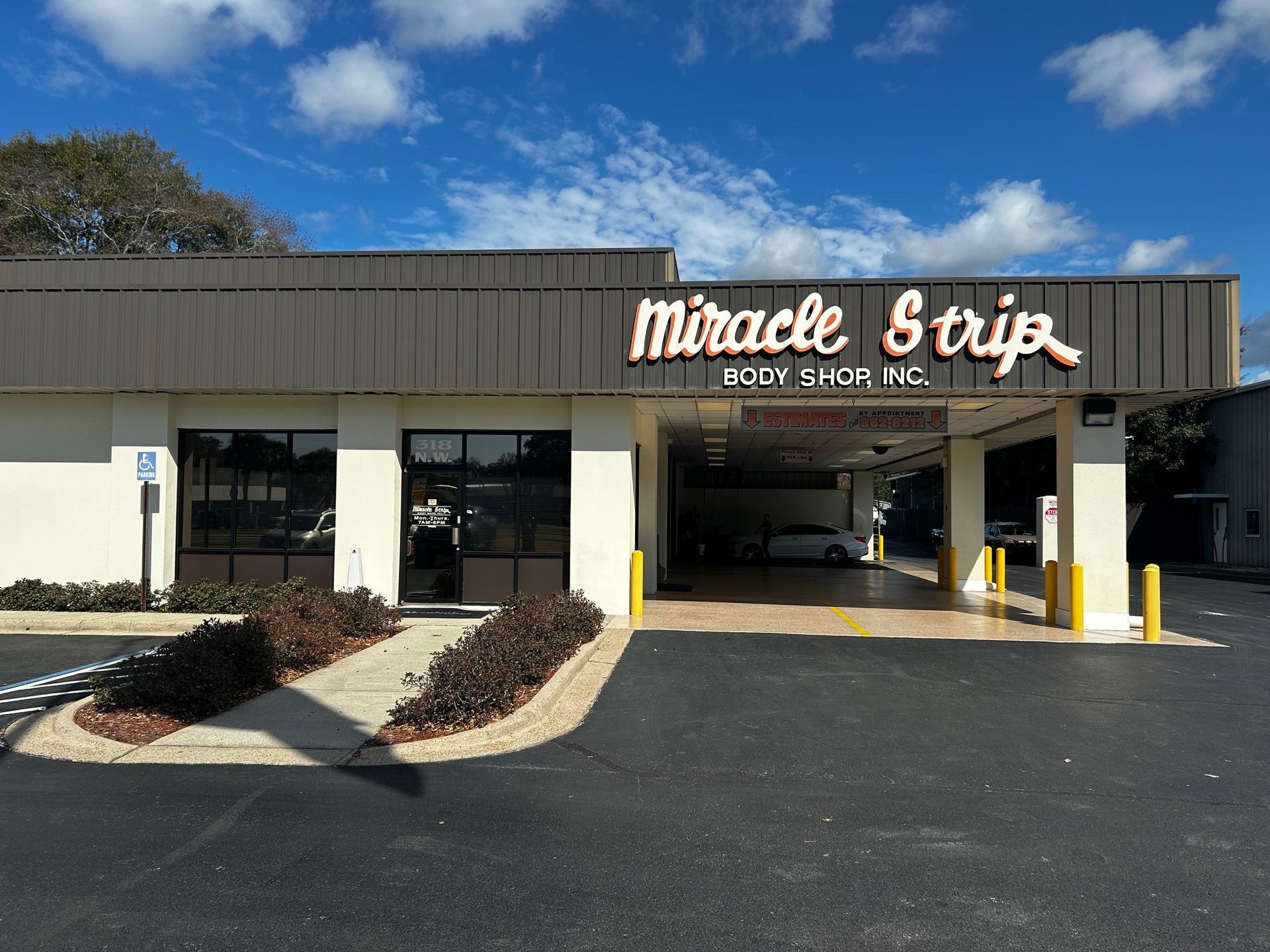 Miracle Strip Body Shop storefront with brown roof, and dark-tinted windows. Entrance to shop is under a covered drive-through.