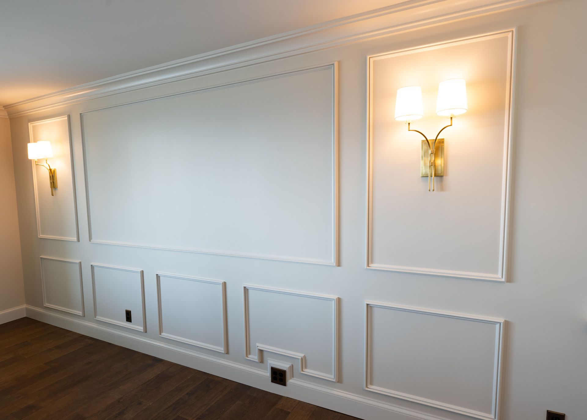 White paneled wall with sconce lighting and brown wooden floor.