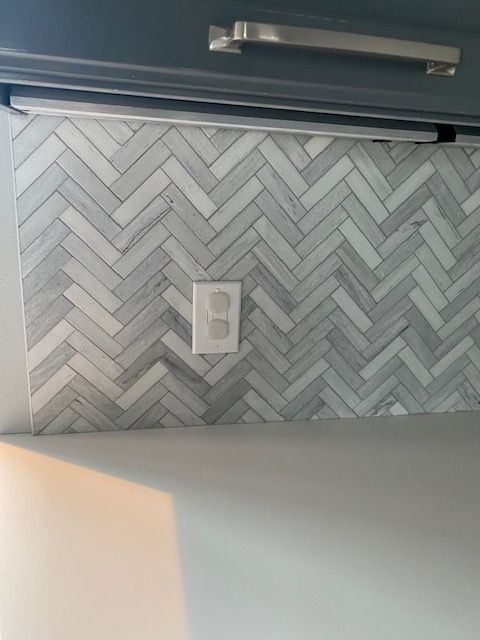 A kitchen with a herringbone tile wall and a light.