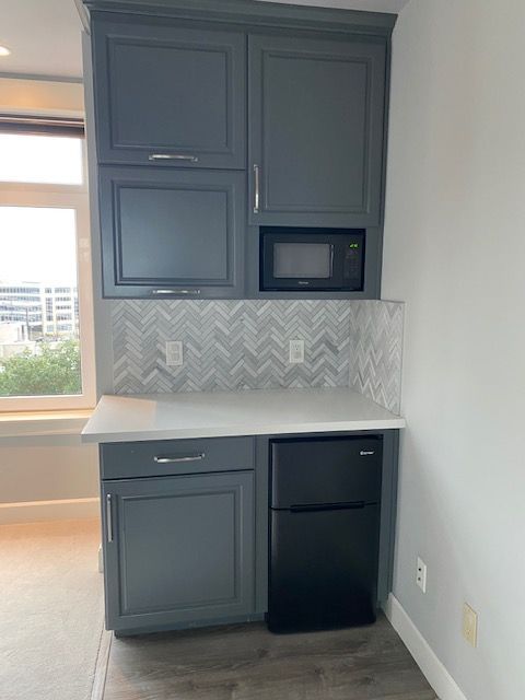 A kitchen with gray cabinets , a black refrigerator , and a microwave.
