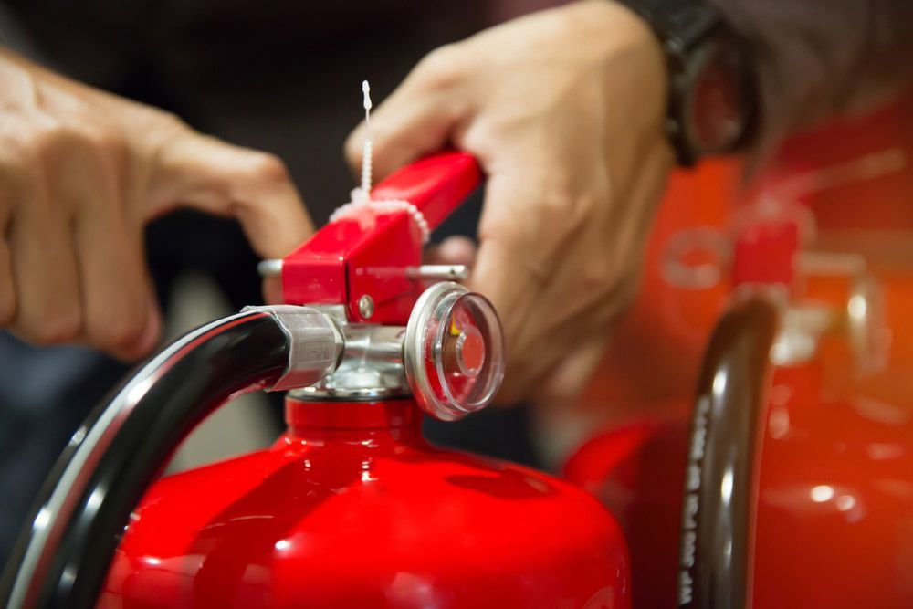 A Person Is Holding A Red Fire Extinguisher In Their Hands — Firewerx In Dubbo, NSW