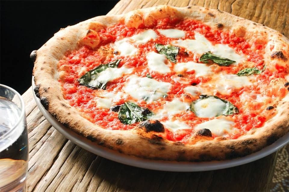 Pizza Margherita su un piatto accanto a un bicchiere d'acqua su un tavolo rustico di legno.