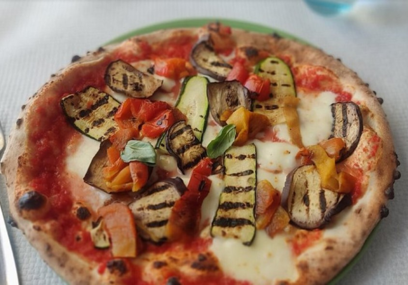 Pizza con verdure grigliate, zucchine, peperoni e formaggio fuso su un piatto bianco.