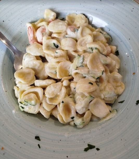 Conchiglie di pasta cremosa alle erbe aromatiche in una ciotola bianca, con un cucchiaio a parte.