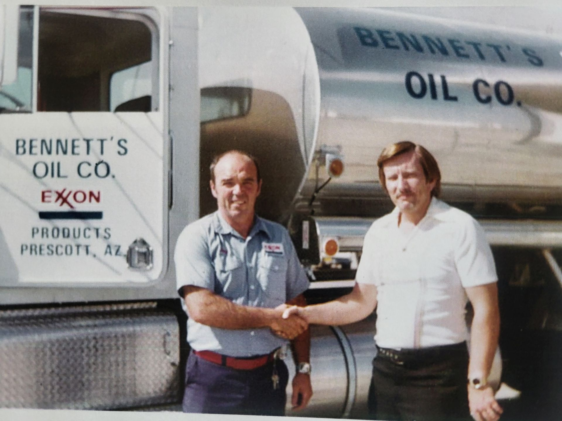 Two men shaking hands in front of a Bennett's Oil Co. truck in Prescott, AZ. The truck is silver.