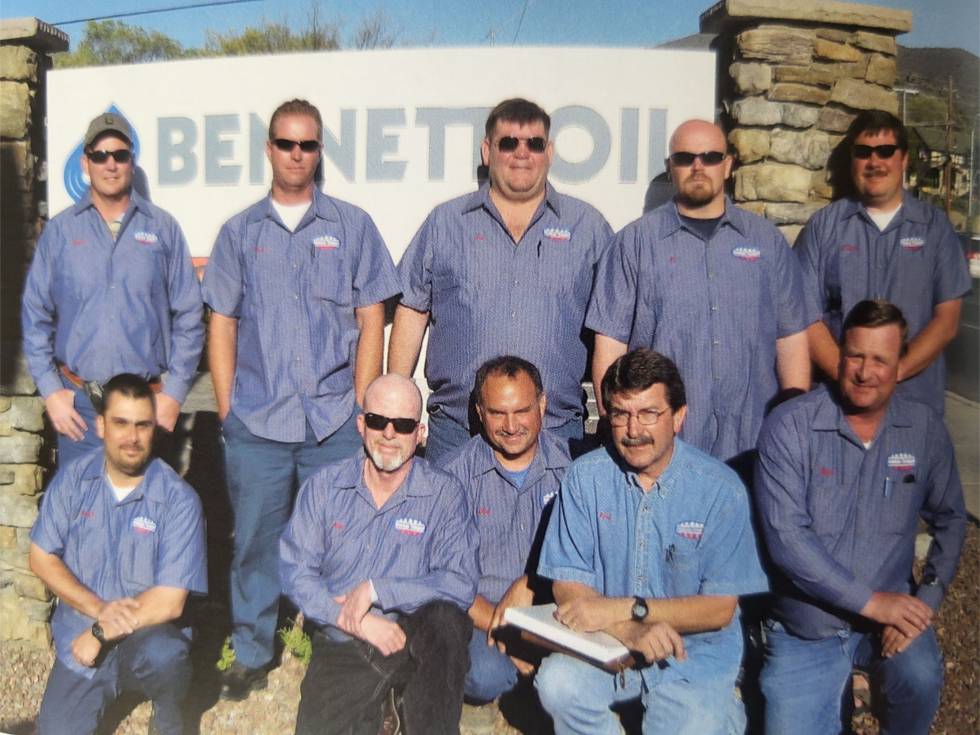 Group of Bennett Oil employees in blue work shirts pose by company sign.