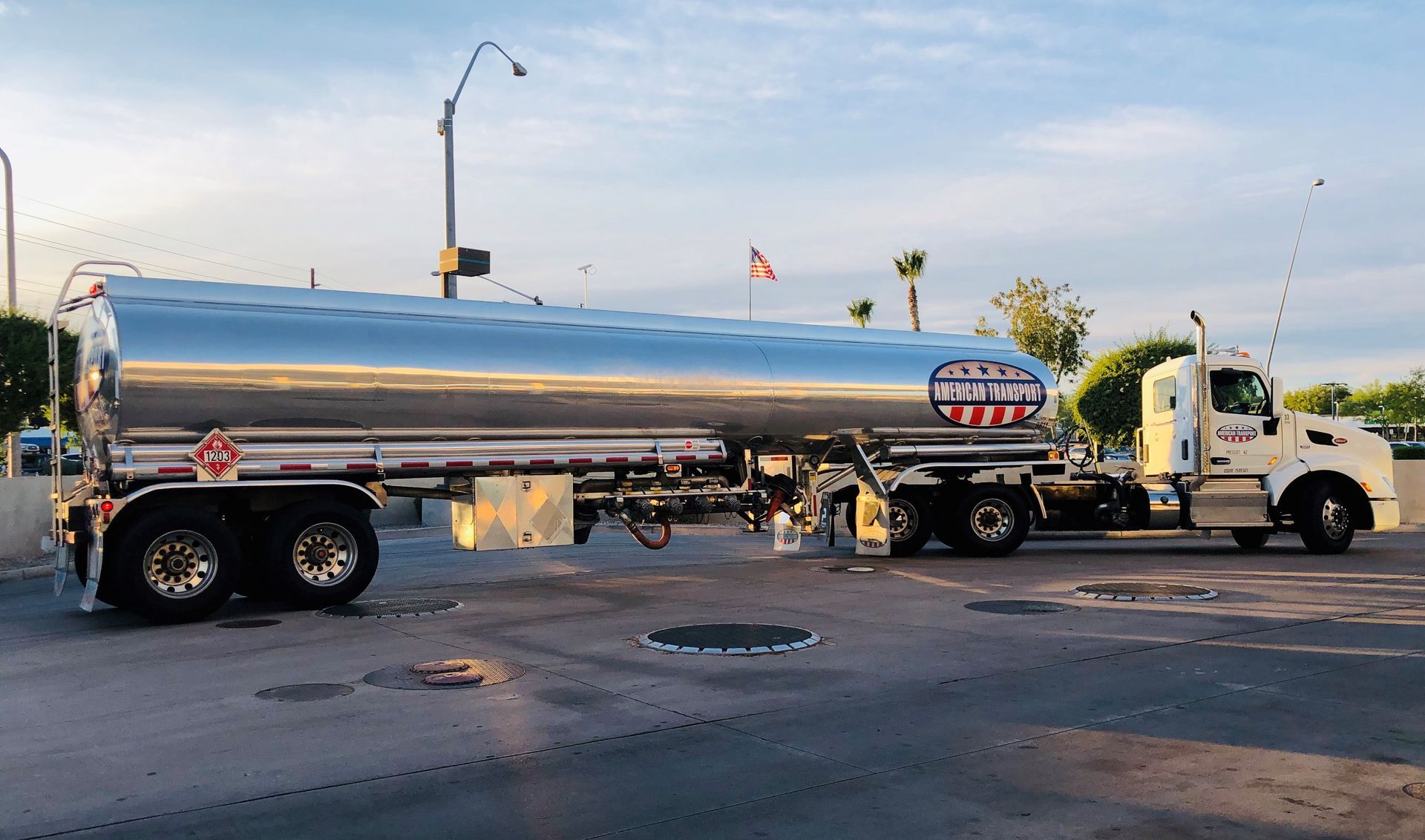 White tanker truck with shiny silver tank parked near a building.