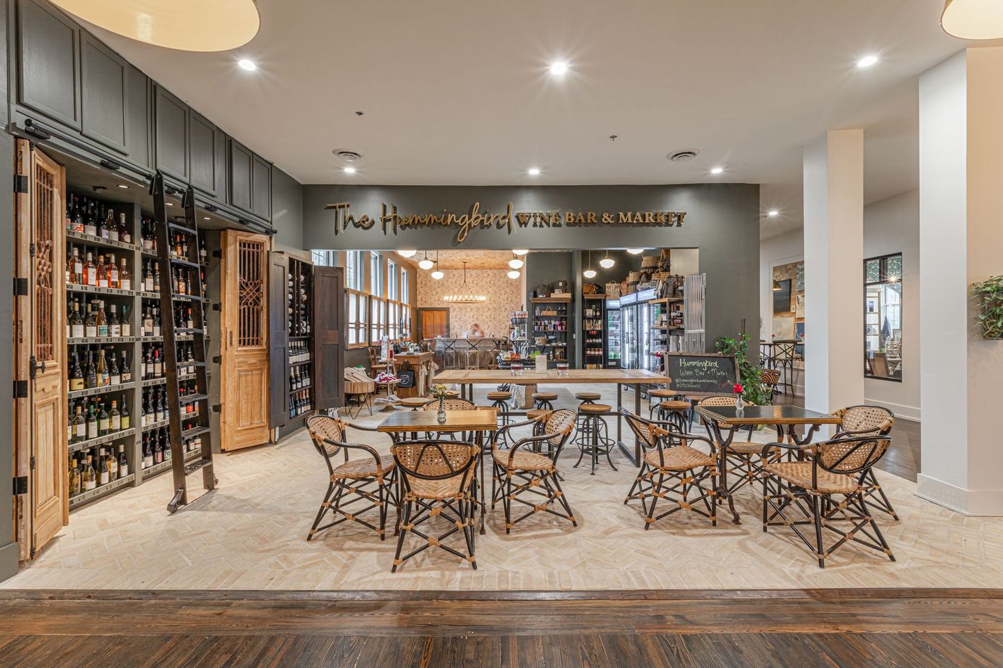 Interior of a restaurant, showcasing wine racks, tables with chairs, and a bar area.