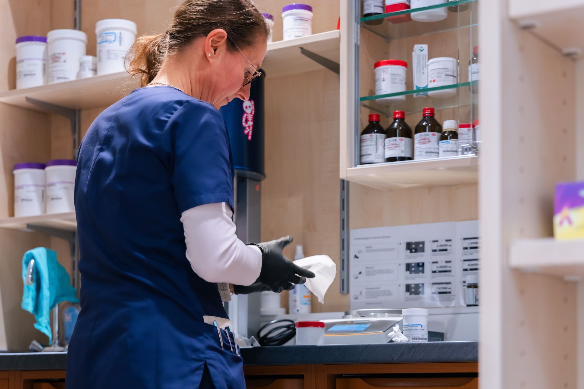 Eine Frau im blauen Kittel arbeitet in einer Apotheke.