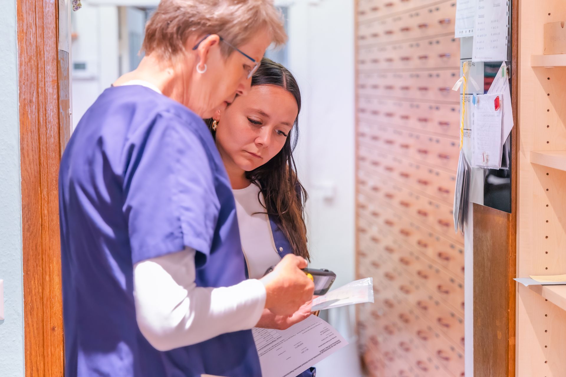 Zwei Krankenschwestern stehen nebeneinander in einem Flur und schauen auf ein Klemmbrett.