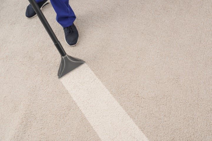 Person using a floor-cleaning tool on a beige carpet, creating a clean white stripe