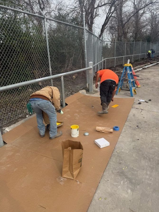 Two workers leveling dirt beside a chain-link fence, with tools and survey equipment on a construction site.