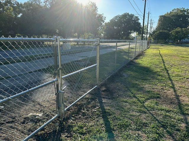 Chain-link fence beside a quiet road, with sunlit grass and long morning shadows.
