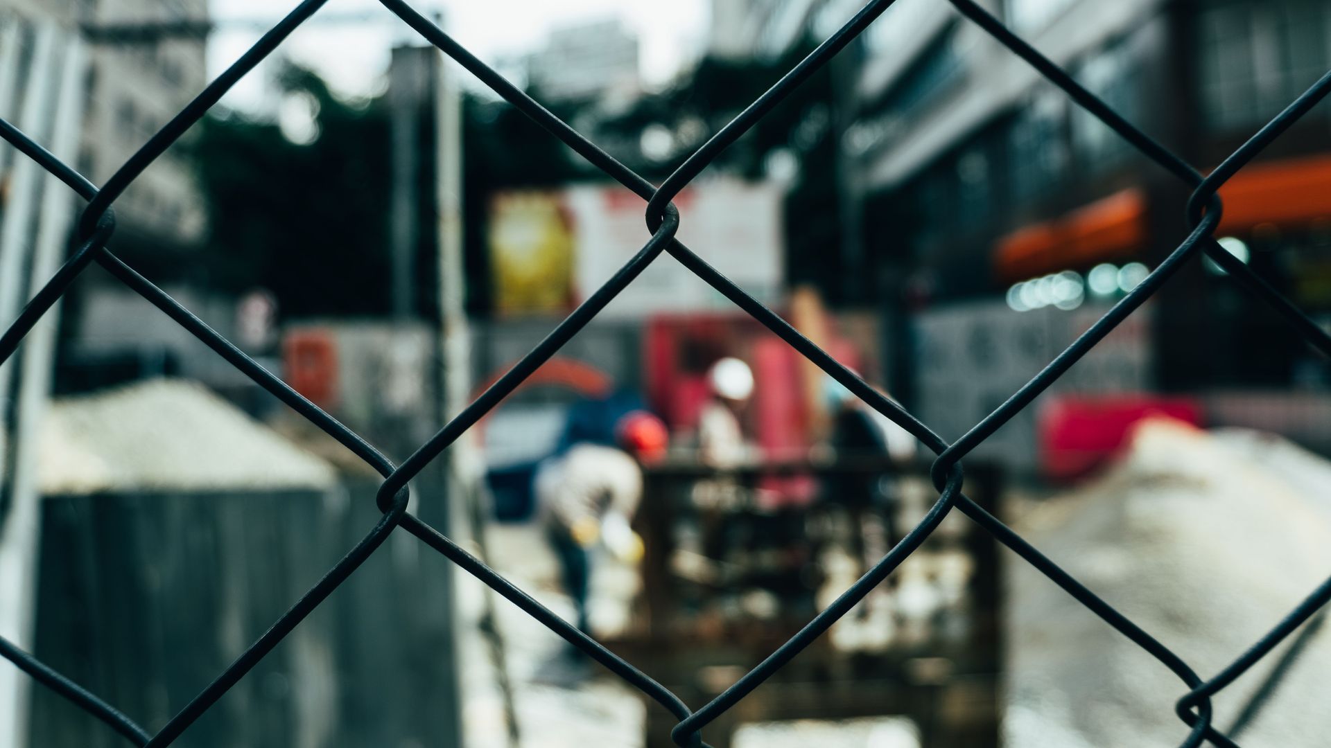 Blurred street scene seen through a black chain-link fence