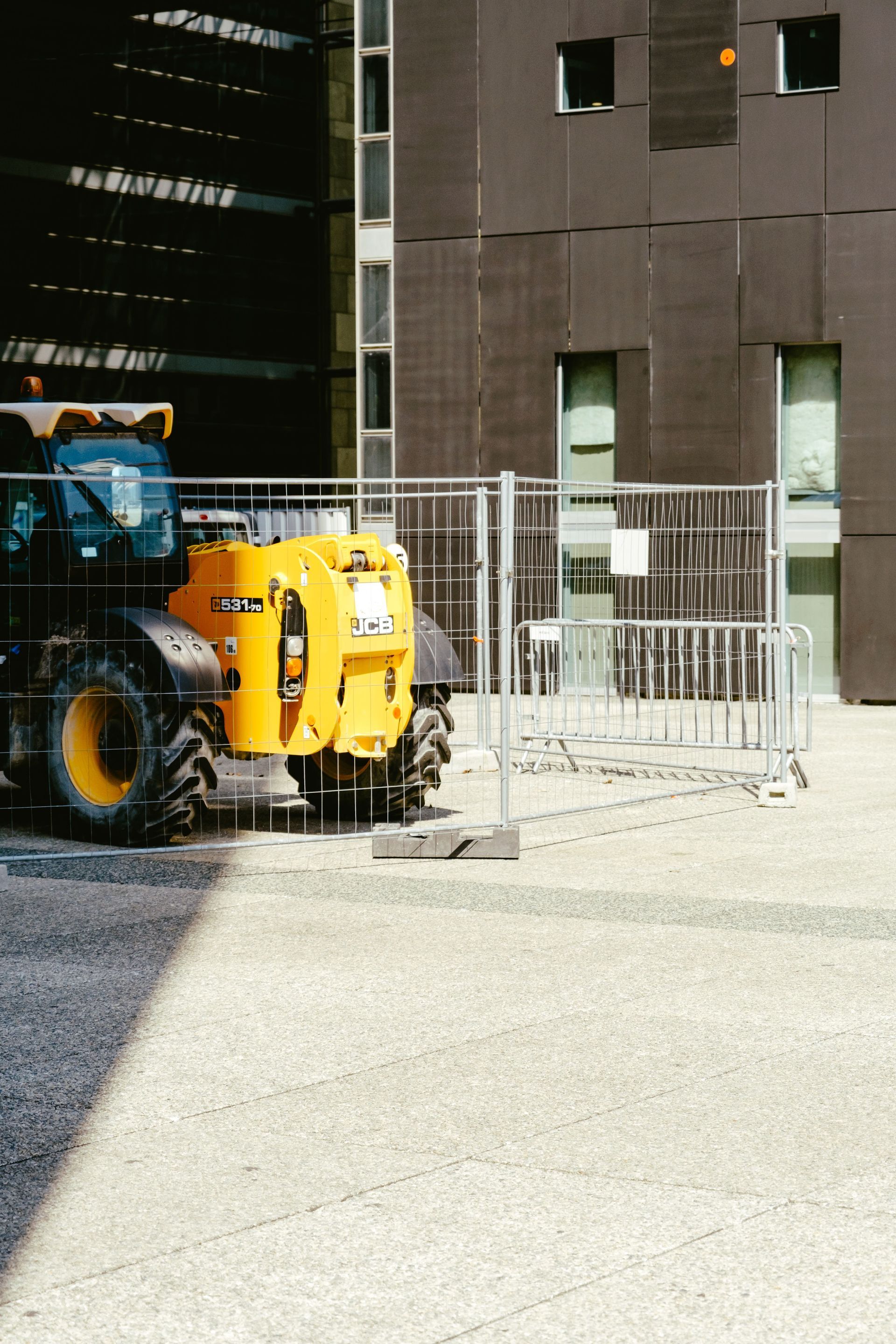 Yellow tractor behind metal fence beside modern building entrance