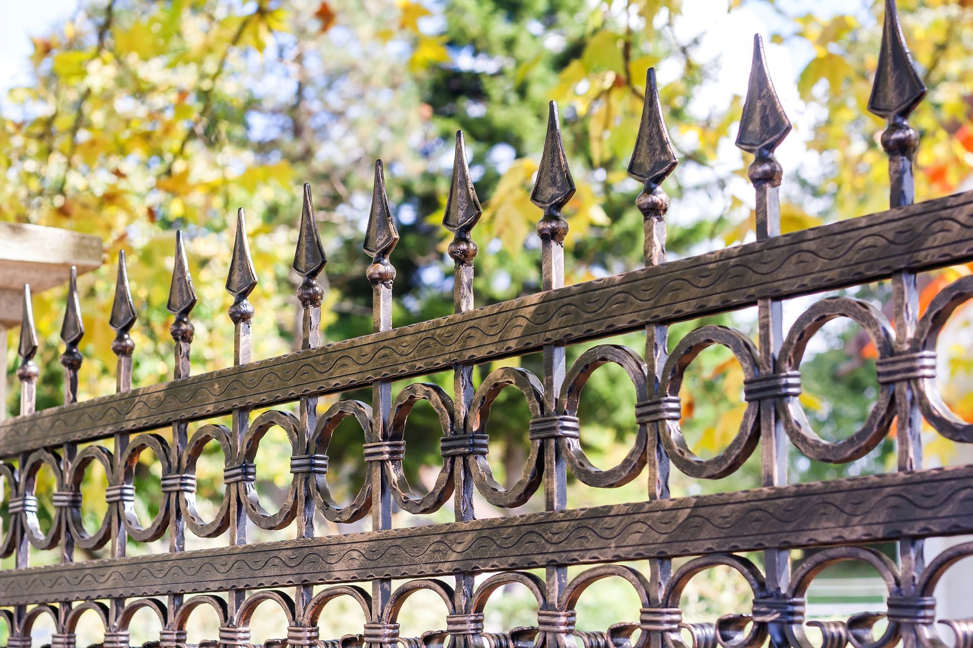 Wrought-iron fence with spear finials and circular details against a blurred green and yellow garden background